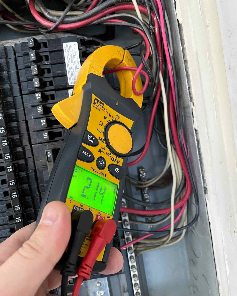A High Mark electrician's clamp meter reading a circuit inside an open breaker panel
